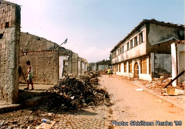 Gjakova's Old Bazaar in ruins in 1999 — gutted, roofless shops along the cobbled street, a few people returning.