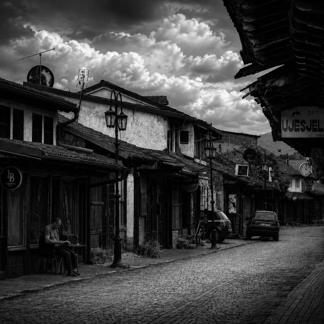 A bazaar lane with a man resting outside a shop under a dramatic sky.